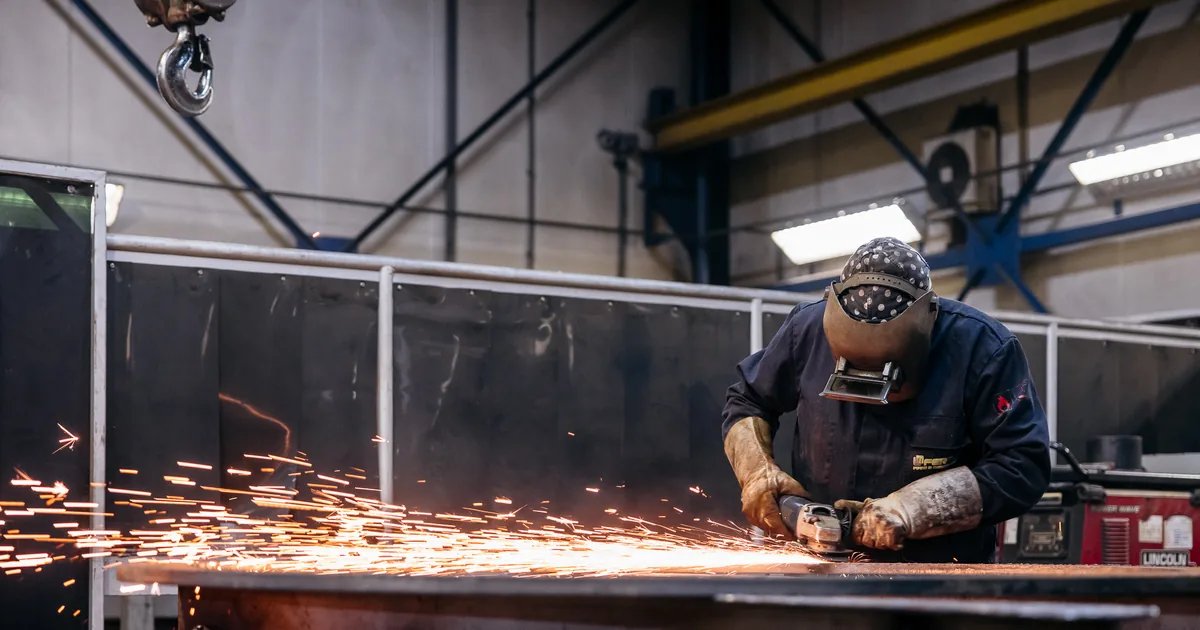 Medewerker slijpt staalconstructie met vonkenregen in industriële werkplaats