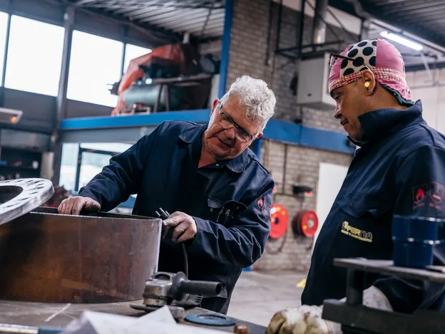 Twee Ferna-medewerkers overleggen over een stalen werkstuk in de werkplaats