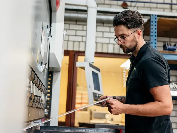 Ferna medewerker inspecteert metaalwerk bij een persbank, kwaliteitscontrole van staal zoals beschreven in het 3.1 certificaat