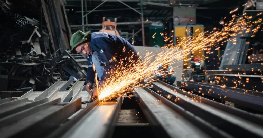 Werknemer slijpt aan staalprofielen met vonkenregen in industriële werkplaats, voorbeeld van materiaalcertificaat staal
