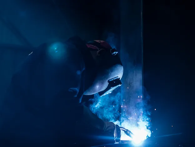 Een lasser is actief bezig met laswerkzaamheden in een donkere industriële omgeving.